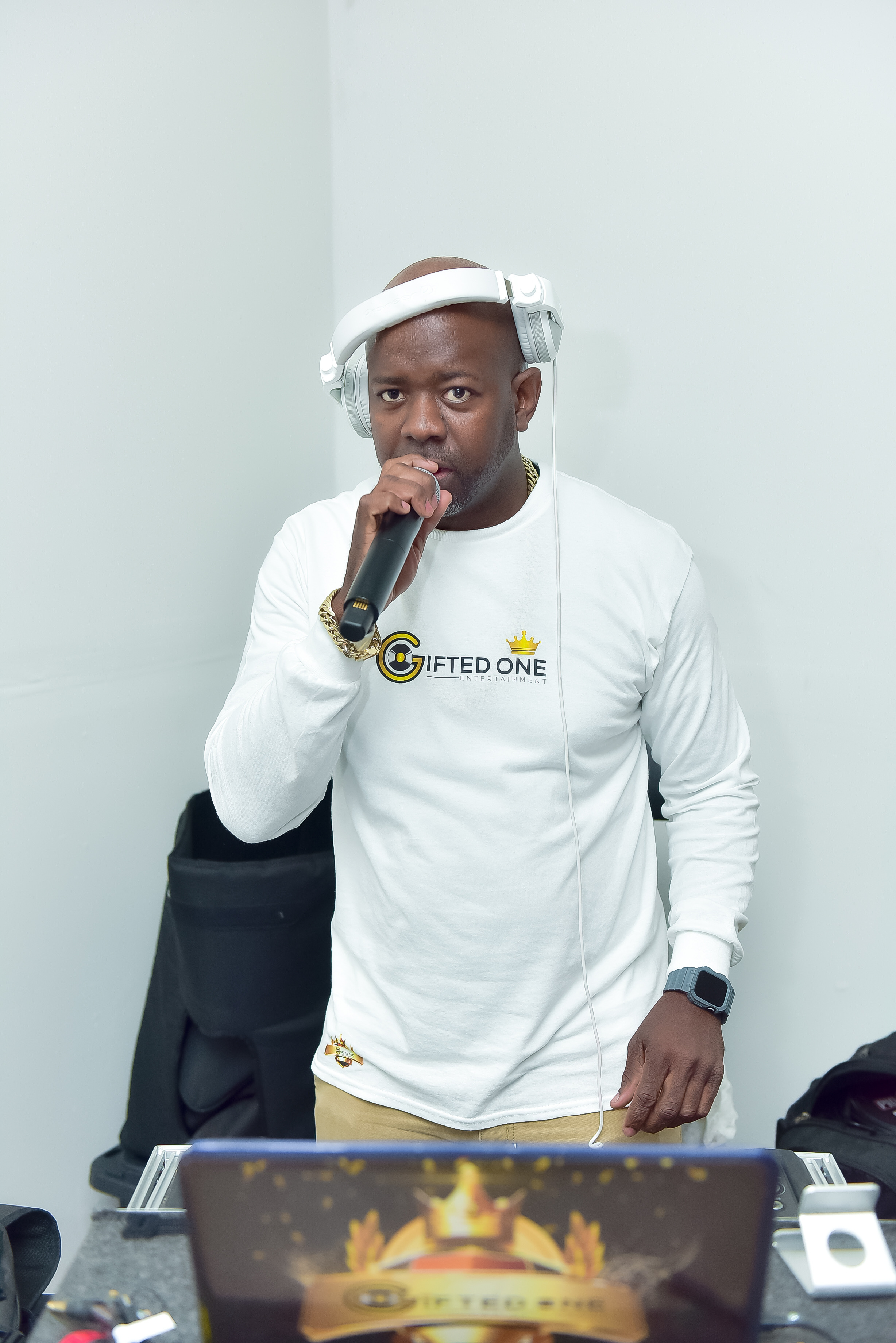 ZJ Gifted wearing white headphones and holding a microphone behind his DJ setup
